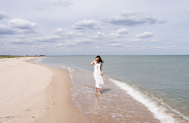 Liberdade jovem com vestido longo branco caminhando na praia