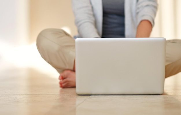Liberdade sem fio em casa Foto recortada de uma mulher usando um laptop enquanto está sentada no chão da sala de estar