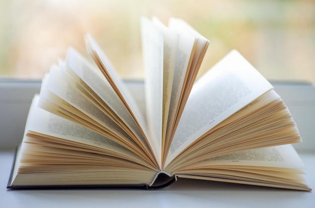 Libro abierto en el alféizar de una ventana iluminada por la luz del sol