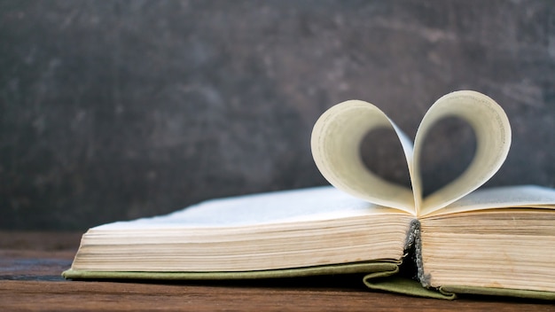 Libro abierto con forma de corazón de una página de papel sobre una mesa de madera oscura.