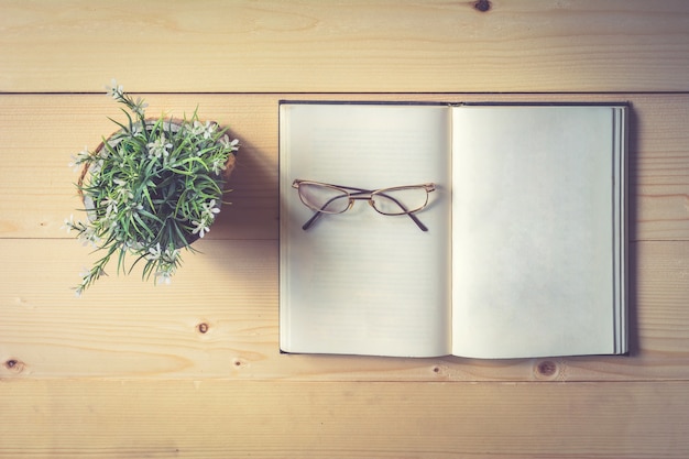 Libro abierto y gafas en la mesa de madera con florero