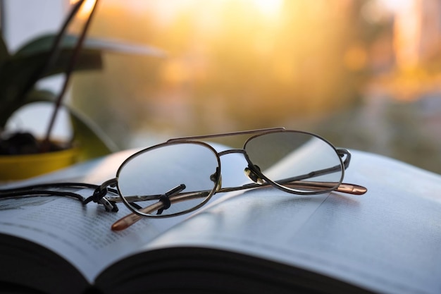 Un libro abierto y gafas yacen sobre la mesa cerca de la ventana con el telón de fondo de la puesta de sol