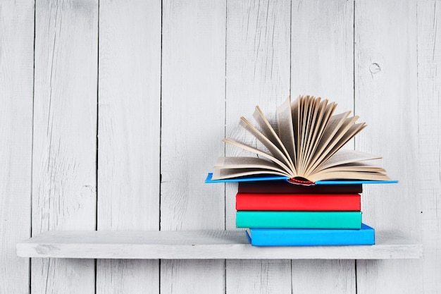 El libro abierto y otros libros multicolores. En un estante de madera. Una mesa de madera blanca.