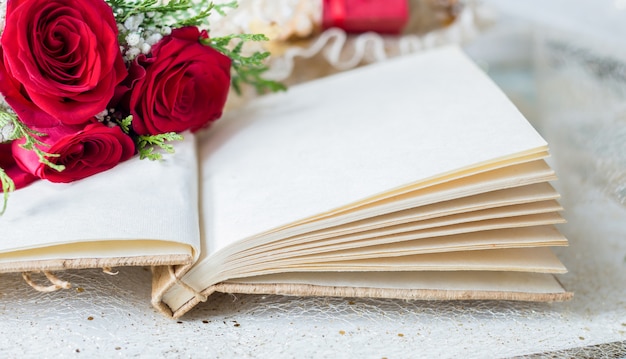 Libro abierto con páginas en blanco y detalle de rosas rojas.