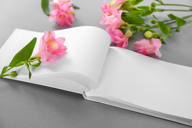 Libro abierto con páginas en blanco y hermosas flores sobre fondo gris