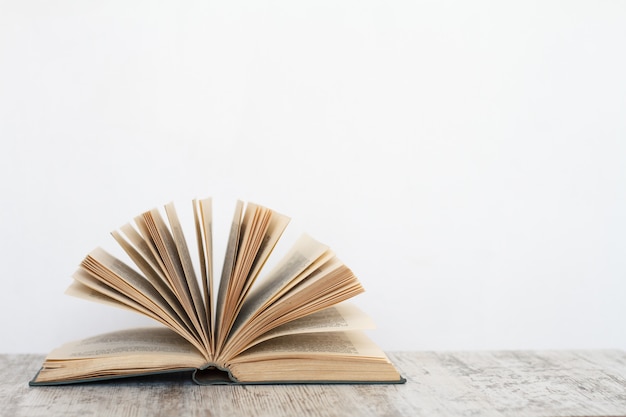 Libro abierto sobre una superficie de madera con el fondo de una pared blanca