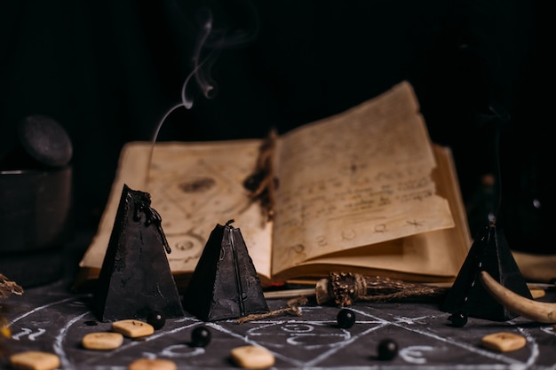 Foto libro antiguo abierto con hechizos mágicos, runas, velas negras en la mesa de brujas. concepto oculto, esotérico, adivinación y wicca. escena de halloween