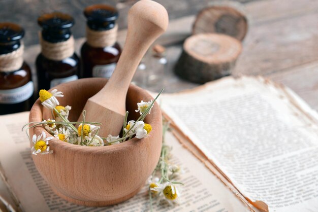 Libro antiguo con flores secas en mortero y botellas en la mesa de cerca