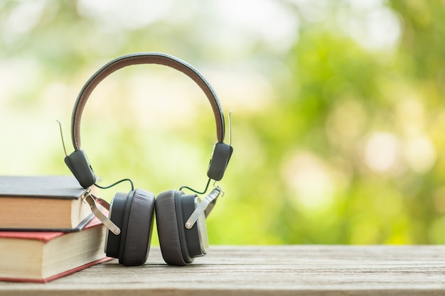 El libro y los auriculares negros en la tabla de madera con la naturaleza verde abstracta empañan. Concepto de lectura y educación