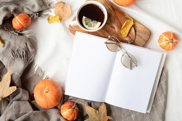 Libro blanco en blanco con hojas de otoño y una taza de té caliente en el diseño de maqueta de libro de mesa