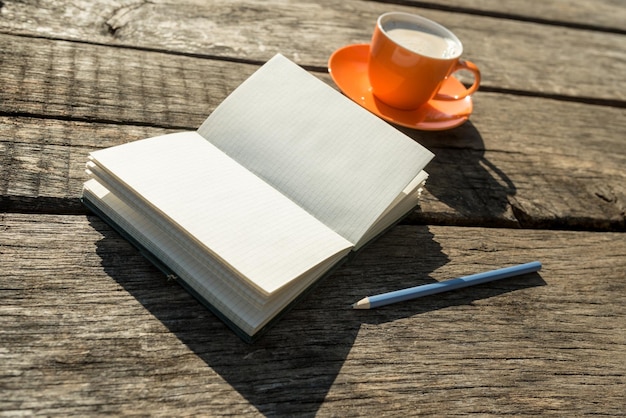 Libro blanco en blanco con lápiz y taza de café sobre una vieja mesa de madera desgastada