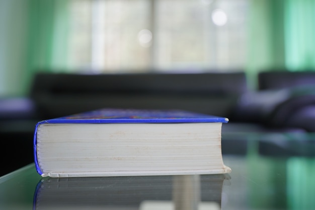 Libro de bolsillo en la mesa de cristal con sofá desenfocado en la habitación