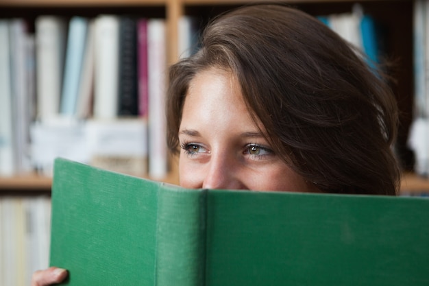 Libro de explotación femenina del estudiante delante de su cara en biblioteca