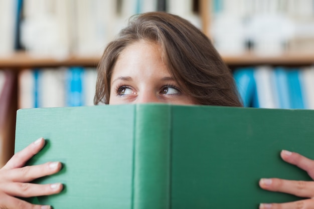 Libro de explotación femenina del estudiante delante de su cara en biblioteca