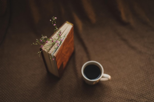 Un libro con flores y una taza de café en la vista superior de fondo oscuro