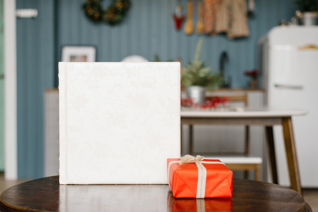 Libro fotográfico de boda blanco con una cubierta de cuero con encaje y una caja roja de regalo de Navidad sobre la mesa