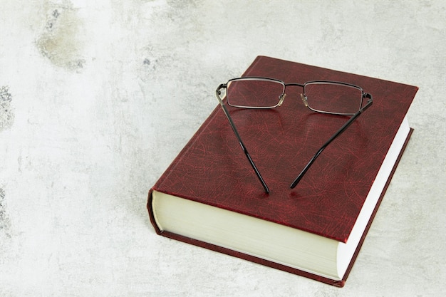 Un libro grueso y gafas en la mesa Un libro y gafas sobre un fondo claro