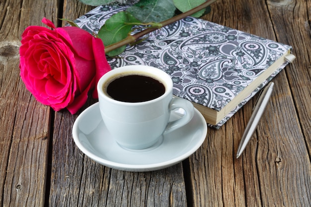 Libro con hermosas rosas y una taza de café en la mesa de madera de cerca