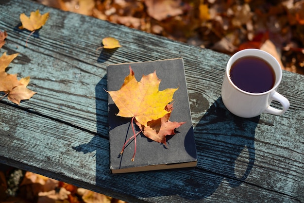 Libro hojas de otoño caídas taza blanca o taza de té o café en el escritorio de madera fondo de otoño al aire libre