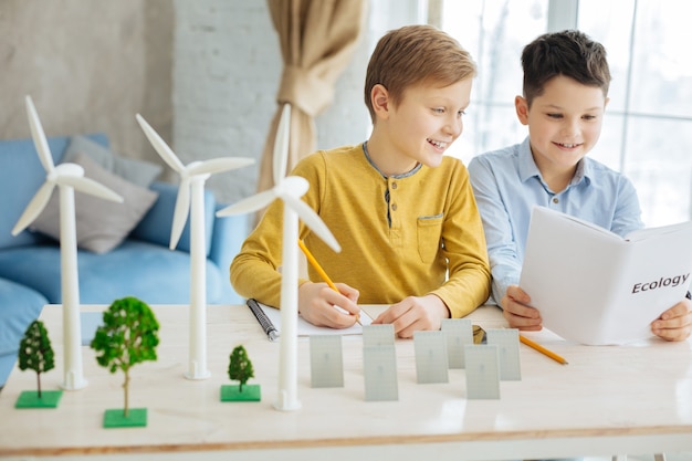 Libro interesante. Niños preadolescentes agradables leyendo el libro sobre ecología para su proyecto escolar mientras uno de los niños toma notas en su cuaderno