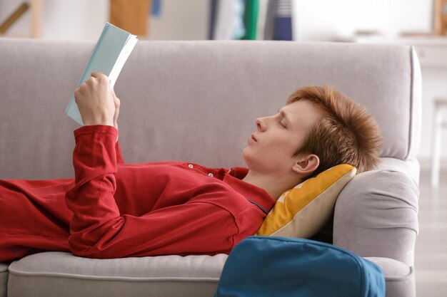 Libro de lectura de adolescente mientras está acostado en el sofá en casa