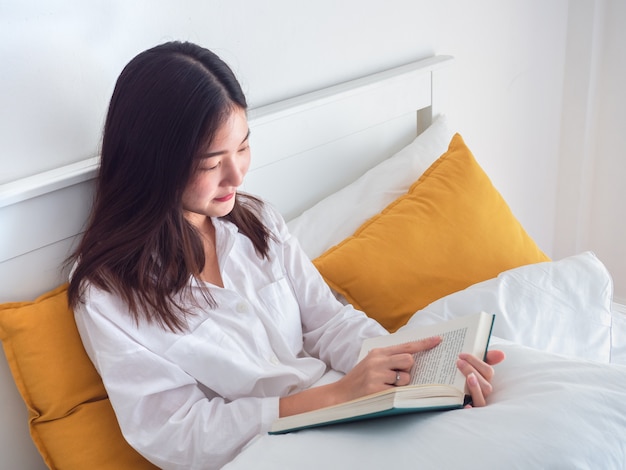 Libro de lectura asiático de la mujer en cama por la mañana