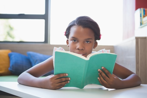 Foto libro de lectura de colegiala en biblioteca