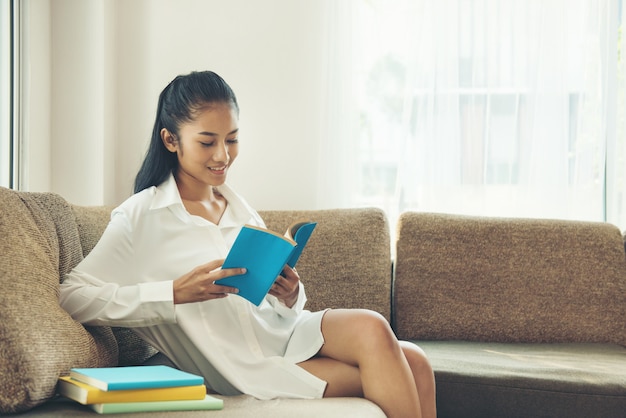 Libro de lectura hermoso de la mujer joven cerca de la ventana en casa