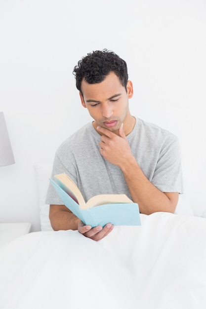 Libro de lectura hombre serio relajado en la cama