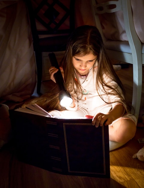 Libro de lectura lindo de la niña debajo de la manta en la noche