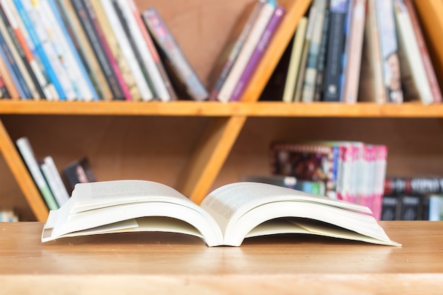 Libro de lectura en la mesa de madera contra el estante.