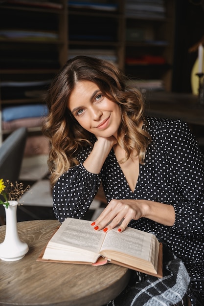 Libro de lectura de mujer joven sonriente mientras está sentado en el café