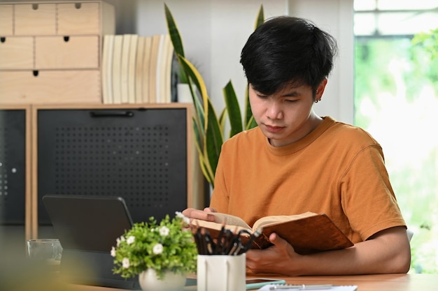 Libro de lectura pacífico joven asiático en la sala de estar.