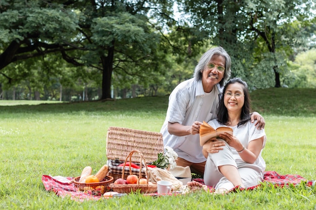 Libro de lectura de pareja senior asiático y picnic en el parque.