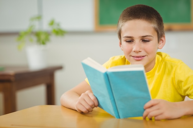 Libro de lectura sonriente del alumno en un aula