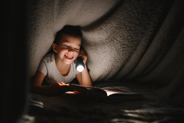 Libro de lectura y uso de linterna. Joven con ropa informal tumbado cerca de la tienda a la hora de la tarde.