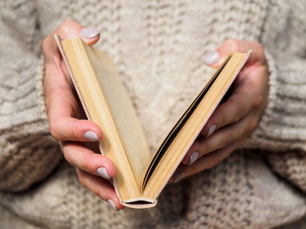 Libro en manos de mujeres. Una niña en un suéter de lana está sosteniendo un libro. Ambiente acogedor