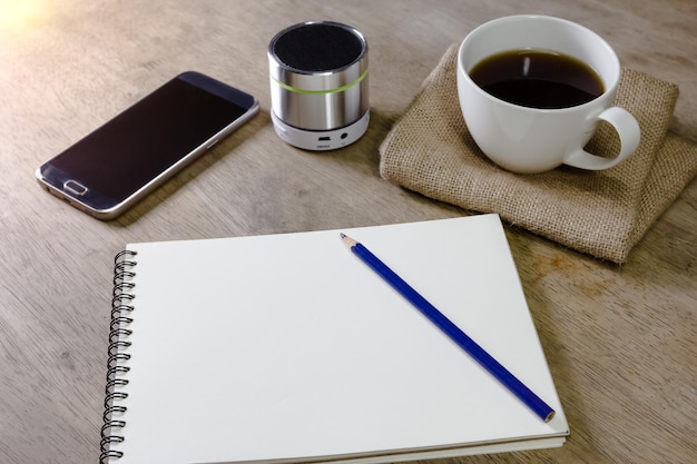 libro de notas con altavoz de lápiz de café y teléfono inteligente en el escritorio