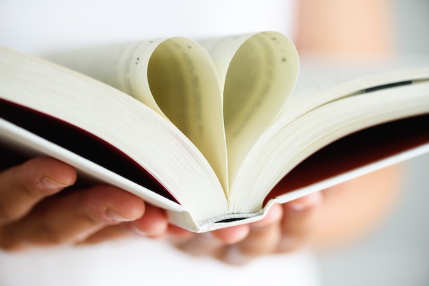 Foto libro con páginas abiertas y forma de corazón en manos de niña.