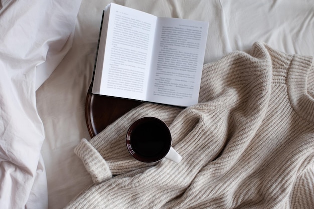 Libro de papel abierto con una taza de café en una bandeja de madera y tejido de tela en la cama vista superior de primer plano Ambiente hogareño acogedor