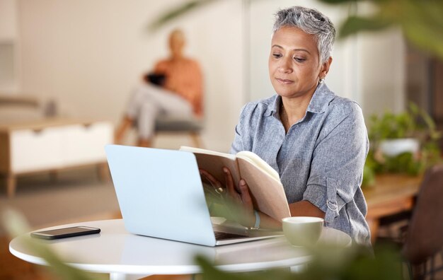 Libro portátil y anciana leyendo mientras investiga para un proyecto en la oficina moderna Café tecnológico y profesional de marketing femenina madura disfrutando de una historia novedosa en su lugar de trabajo