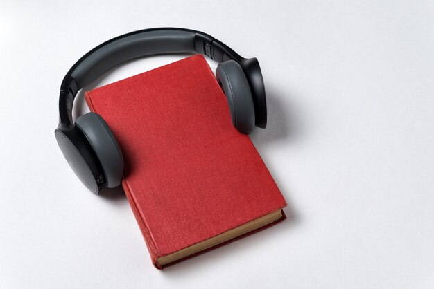 Libro rojo con auriculares sobre fondo blanco. Aprendizaje con el concepto de audiolibro. Copia espacio