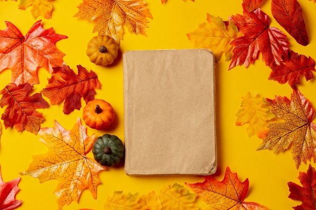 Libro romántico y calabaza con hojas de otoño sobre fondo amarillo. Vista superior