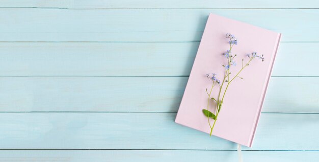 Libro rosa o cuaderno con una ramita de nomeolvides sobre un fondo de madera azul claro