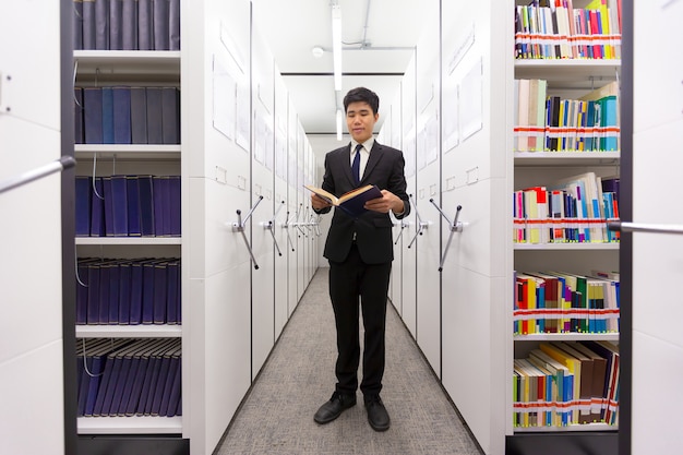 Libro secreto de la lectura del hombre de negocios que busca conocimiento en un sitio seguro de la biblioteca del armario con el va