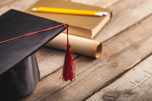 Libro de sombrero de graduación y diploma sobre fondo de madera