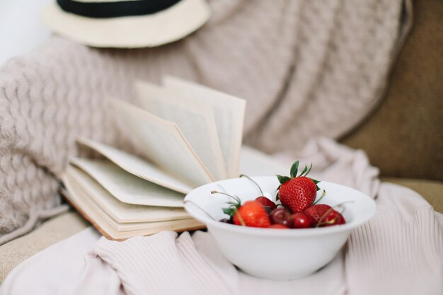 Libro de sombrero de traje de baño y cerezas y fresas frescas sobre superficie de madera