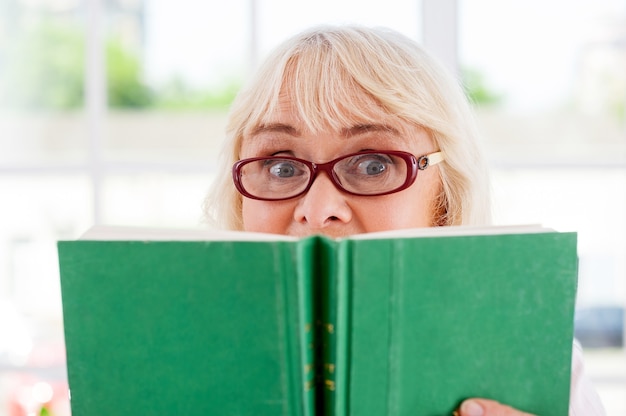 ¡Libro tan emocionante! Mujer senior sorprendida sosteniendo un libro y mirando hacia afuera