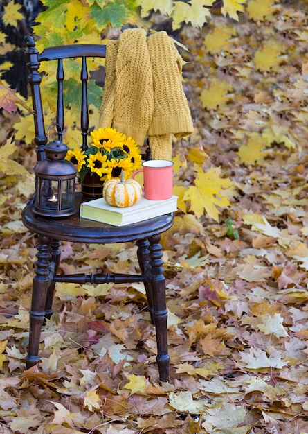 Un libro, una taza, una calabaza, junto a él hay un ramo de girasoles y una vieja linterna en el jarrón, un suéter de punto amarillo.