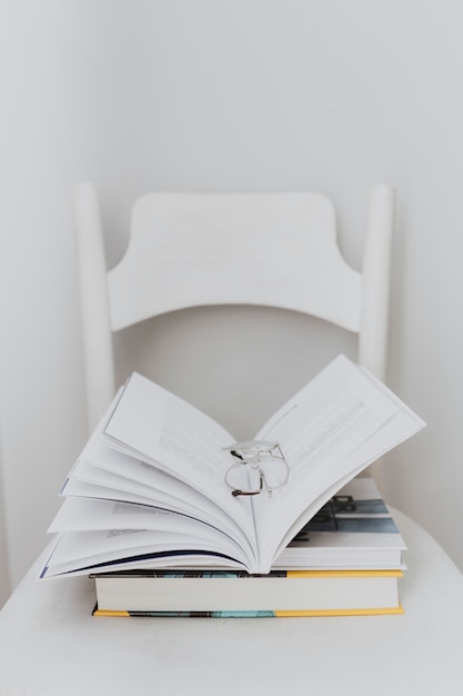 Foto libro de texto abierto y un par de gafas en una silla blanca